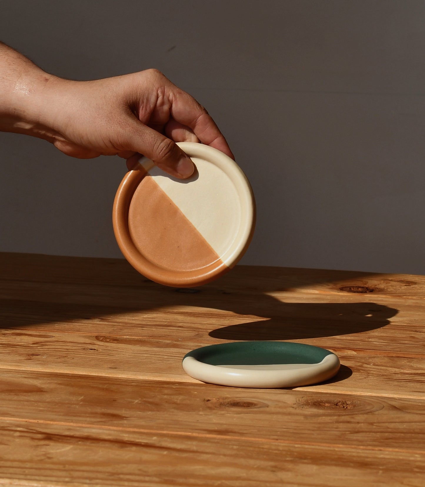 Ceramic candle coasters, front view with a hand holding one above a table.