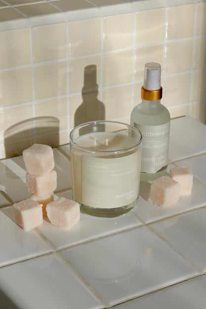 Sanctuary Candle and room spray on a tiled bathroom counter, side view.