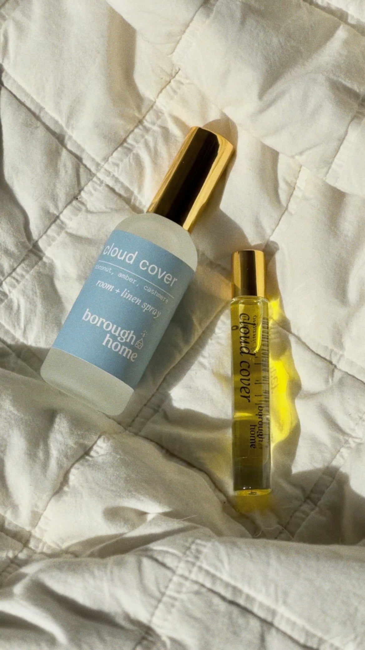 Cloud cover perfume rollerball and room spray on a bed, top down view.