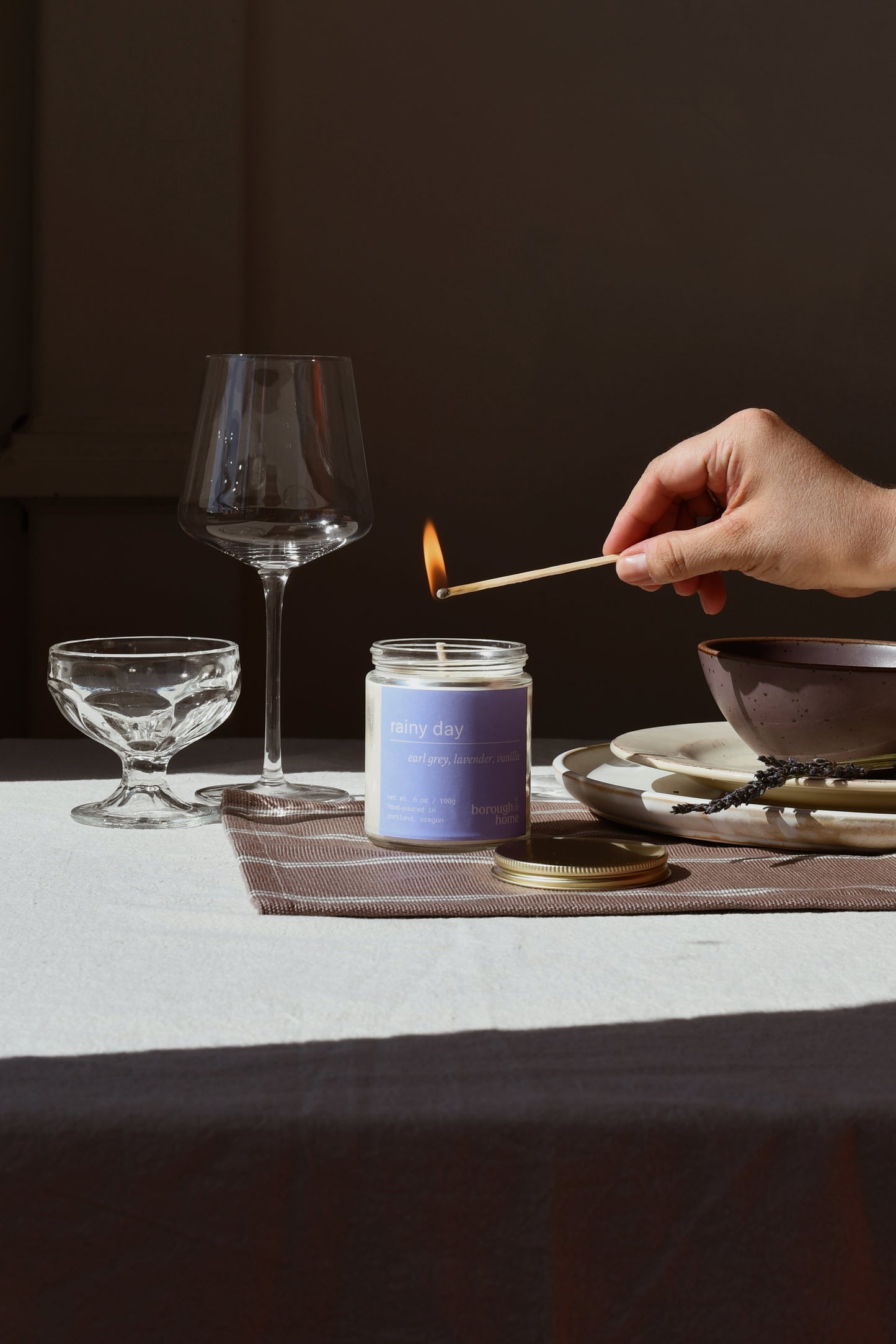 Rainy Day candle being lit with a match on a table, front view.