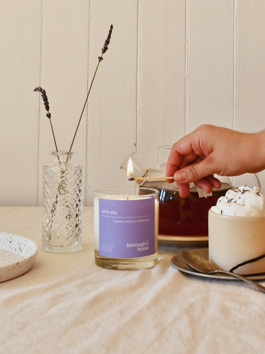 Rainy Day candle being lit next to a pot of tea, front view.